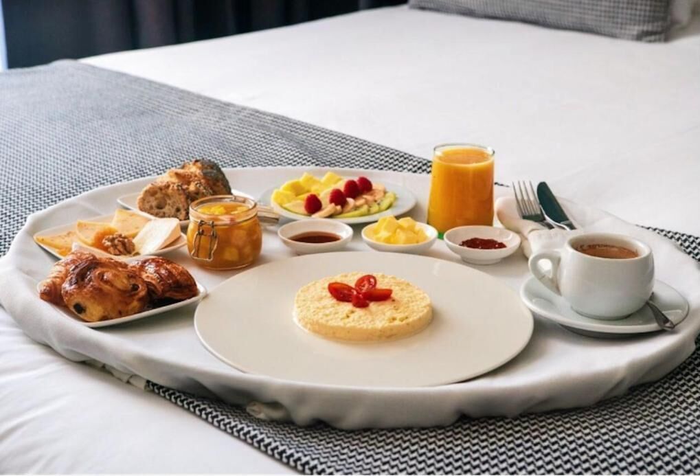 A breakfast tray with croissants, fruit, a cookie, and coffee on a bed.