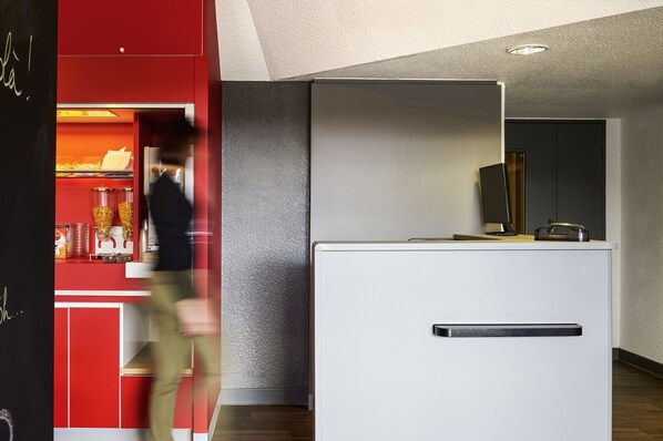 A modern kitchen with a red and white color scheme, a white countertop, and a built-in oven. - hotelF1 Lyon Sud Oullins (Oullins)