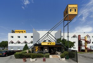 A hotel with a modern design, featuring a prominent 'hotel F1.com' sign, a well-maintained garden, and a clear sky. - hotelF1 Lyon Sud Oullins (Oullins)