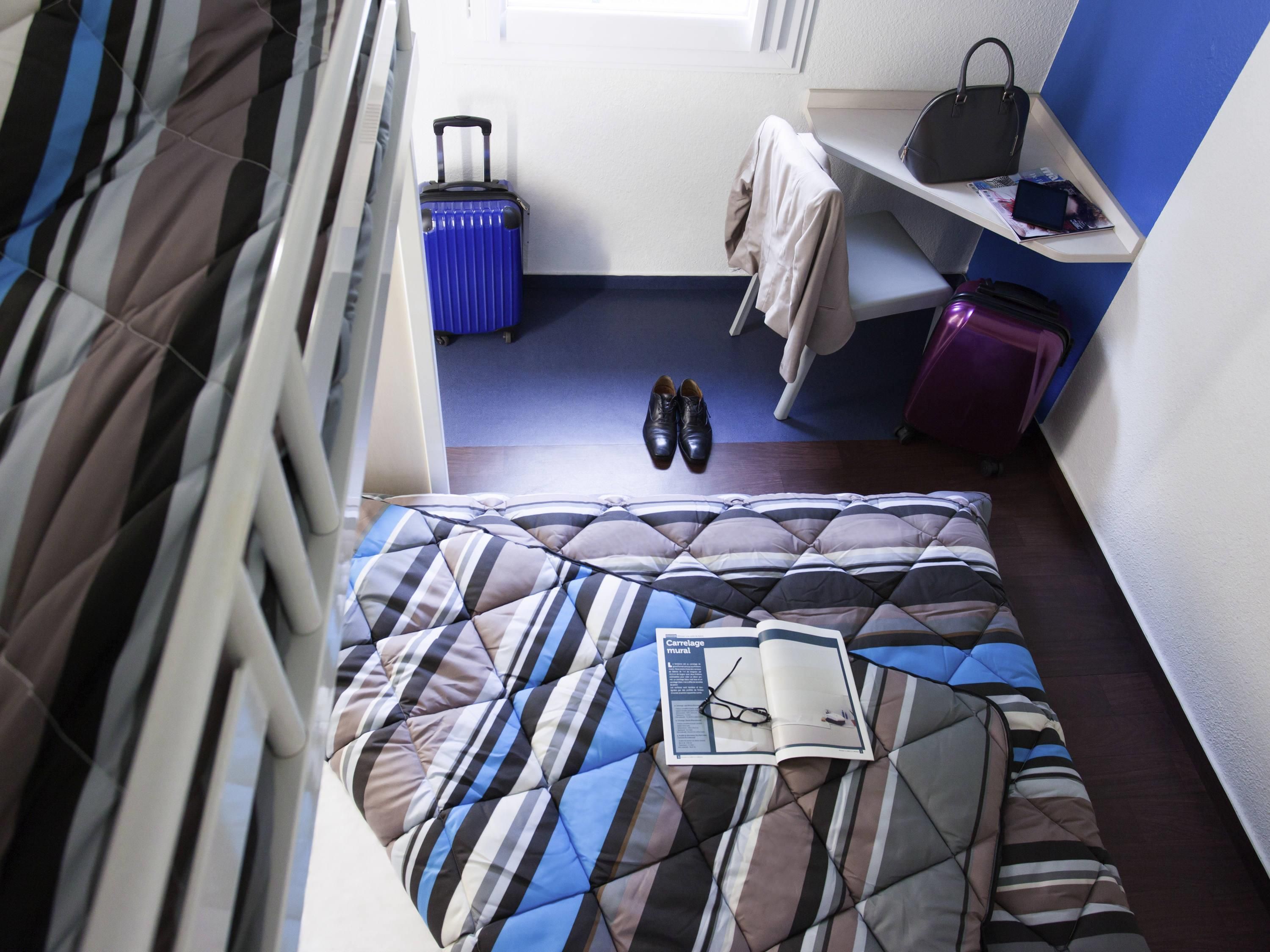 A bed with striped bedding, a pair of shoes, a book, and a suitcase on the floor.