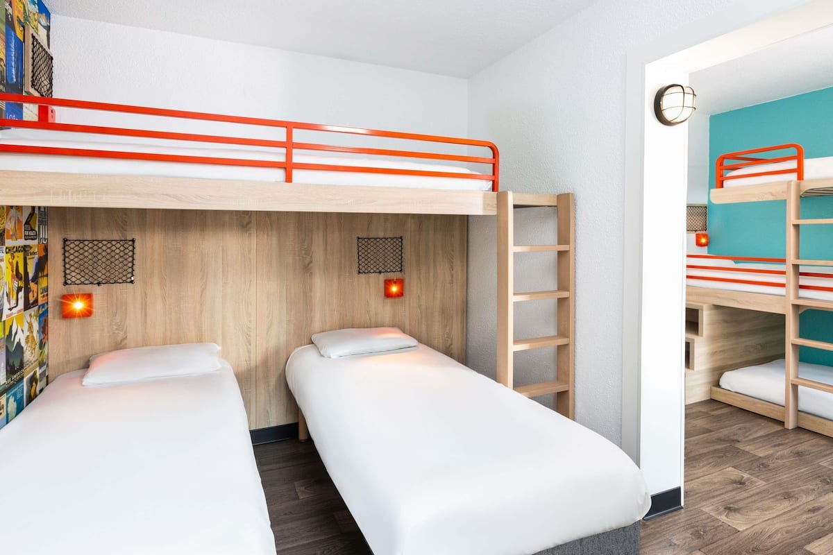 A room with two single beds, a bunk bed, wooden flooring, and a wall-mounted light fixture.