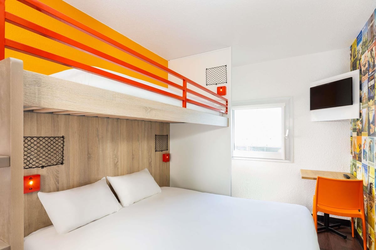 A bedroom with a bunk bed, a desk with a chair, a TV, and a window.