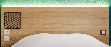 Una cama con colchón blanco, cabecera de madera, una mosquitera negra y dos interruptores fijados a la pared.