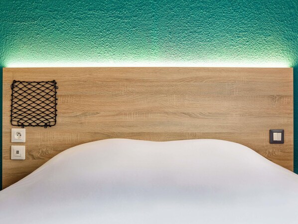 A bed with a white mattress, a wooden headboard, a black netted item, and two wall-mounted switches. - hotelF1 Poitiers Nord Futuroscope (Chasseneuil-du-Poitou)