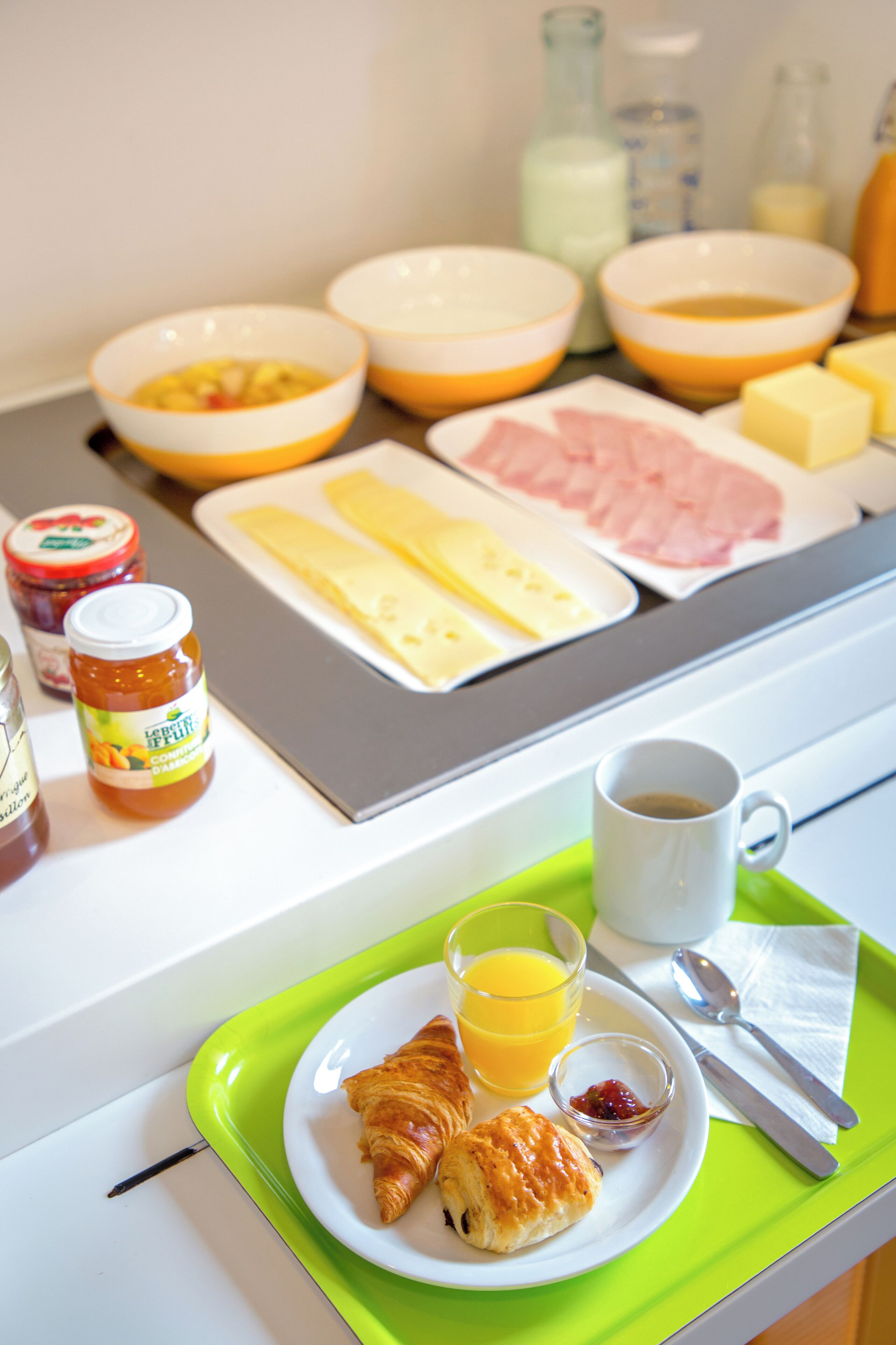 Bandeja de desayuno con cruasanes, zumo de naranja, mermelada, mantequilla y botes de confitura.