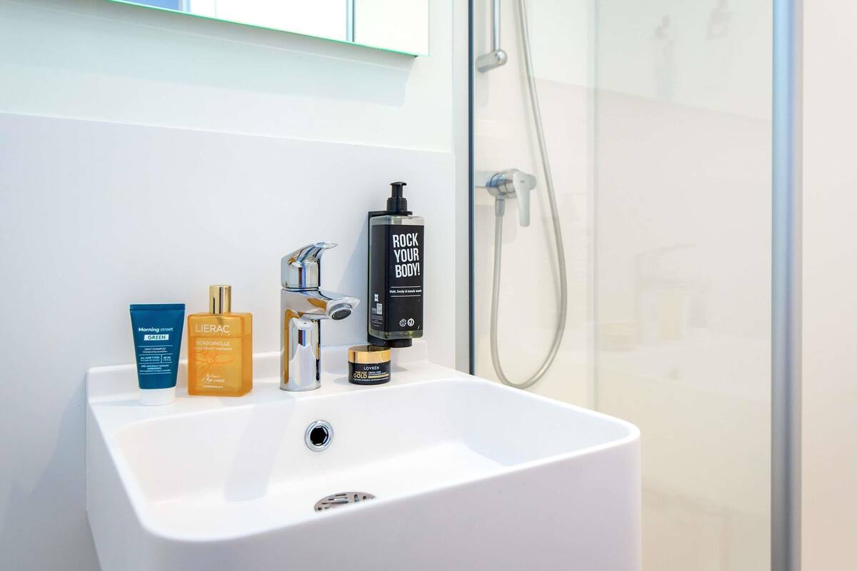Un baño con lavamanos blanco, espejo y ducha.
