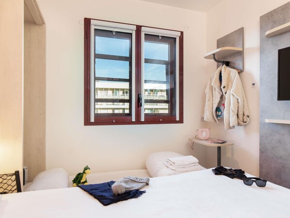 A hotel room with a bed, a window, a wall-mounted shelf with a lamp, and a view of a building outside. - ibis budget Perpignan Centre Méditerranée (Perpignan)