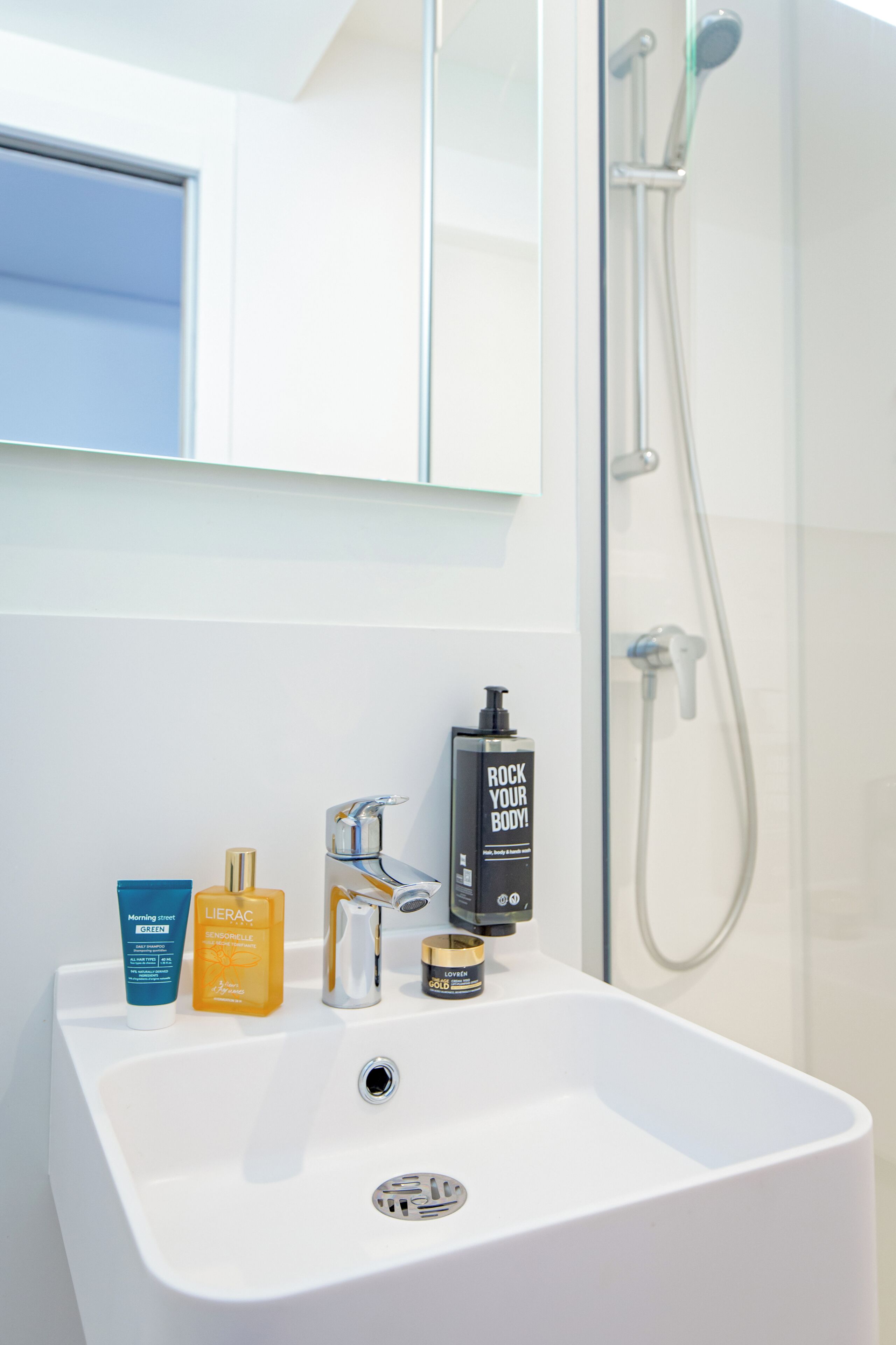 Une salle de bain avec un lavabo blanc, un miroir et une douche.