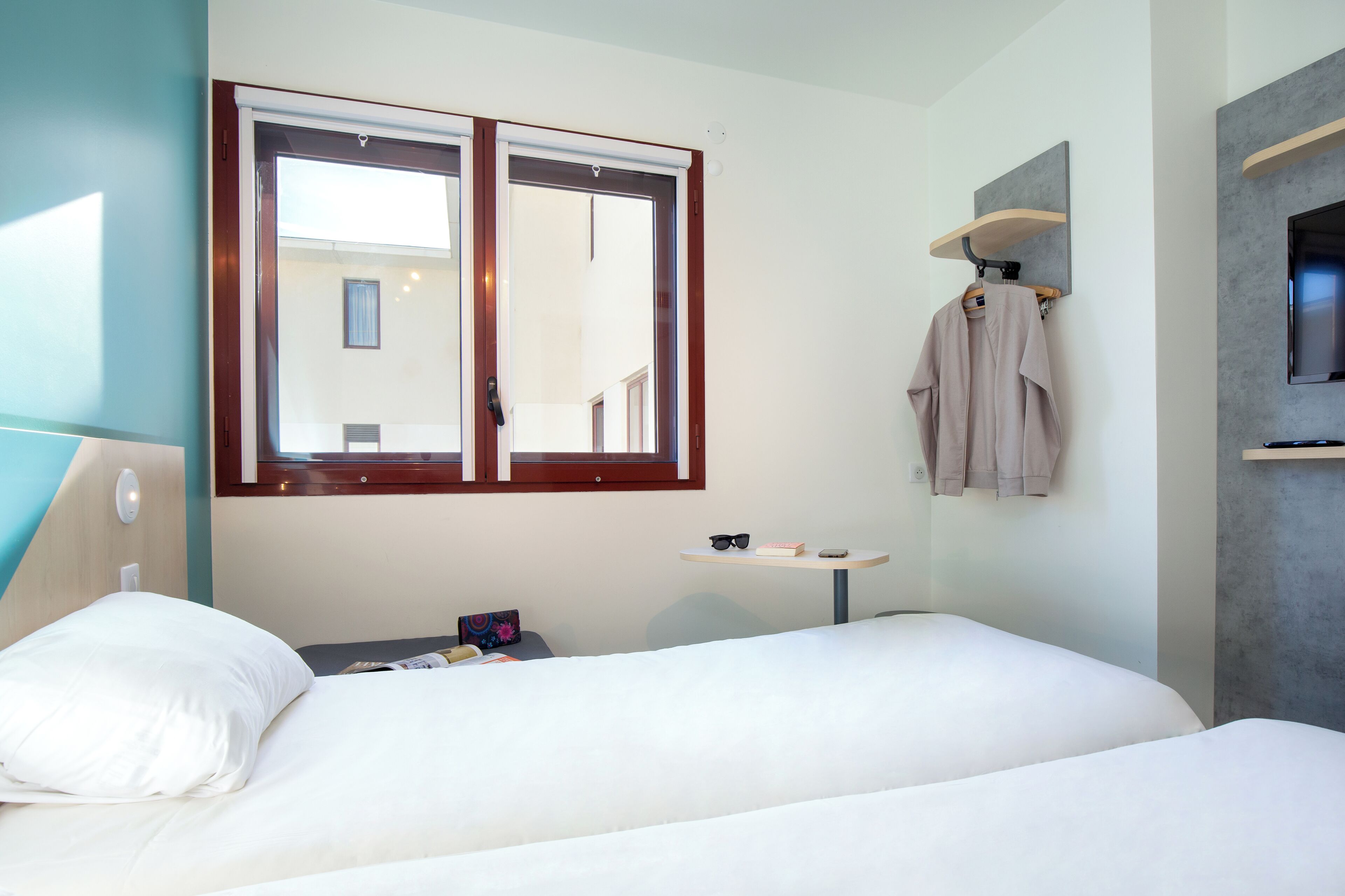 Habitación de hotel con cama, una mesita con un par de gafas de sol, toallero con toalla y televisor montado en la pared.
