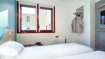Habitación de hotel con cama, una mesita con un par de gafas de sol, toallero con toalla y televisor montado en la pared.