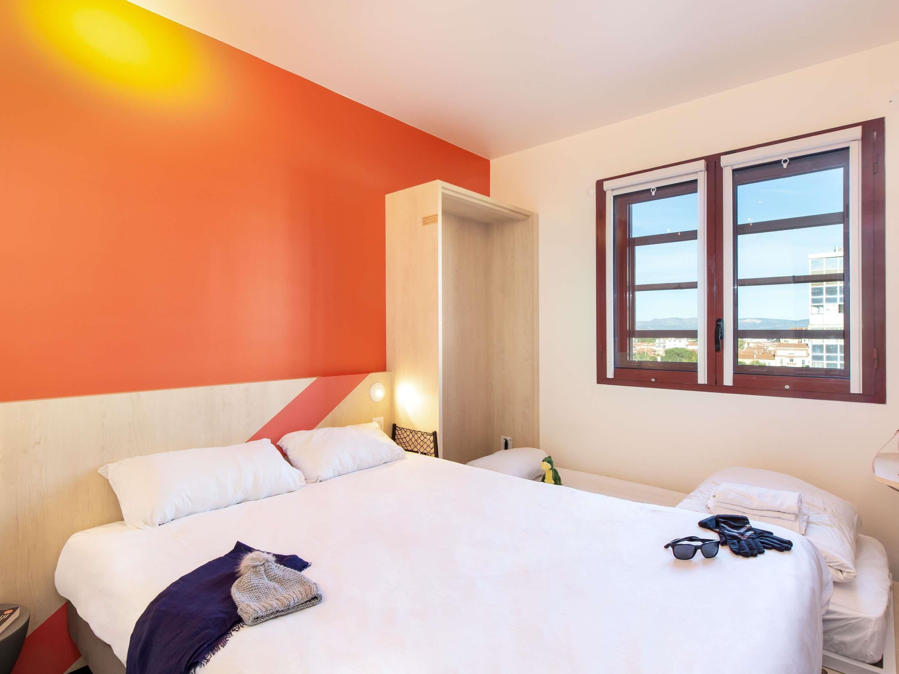 A hotel room with a large bed, a smaller bed, a window with a view, and a door leading to another room.
