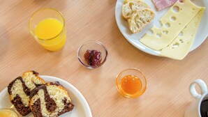 Una mesa de desayuno con croissants, jamón, queso, pan, dátiles y un vaso de zumo de naranja.