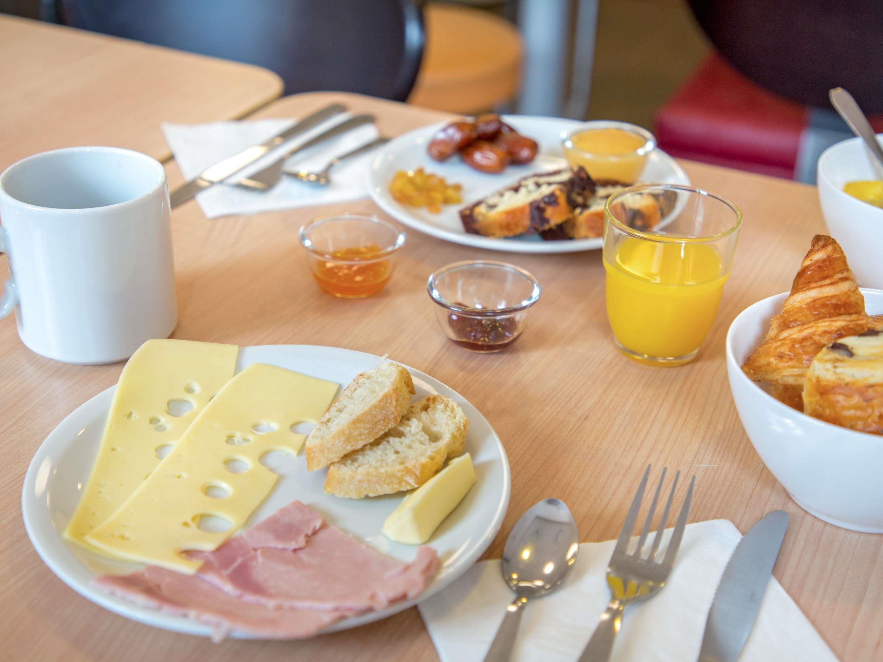 Una mesa de desayuno con queso, jamón, pan, cruasanes y jugo de naranja.