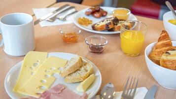 Una mesa de desayuno con queso, jamón, pan, cruasanes y jugo de naranja.