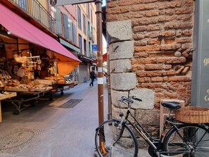 Una calle estrecha con un puesto de mercado a la izquierda y un muro de ladrillo a la derecha.