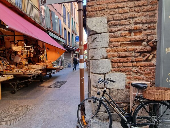 Una calle estrecha con un puesto de mercado a la izquierda y un muro de ladrillo a la derecha.