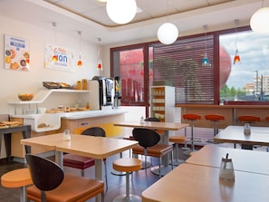 A modern dining area with tables and chairs, a coffee machine, and a window with a view. - ibis budget Perpignan Centre Méditerranée (Perpignan)