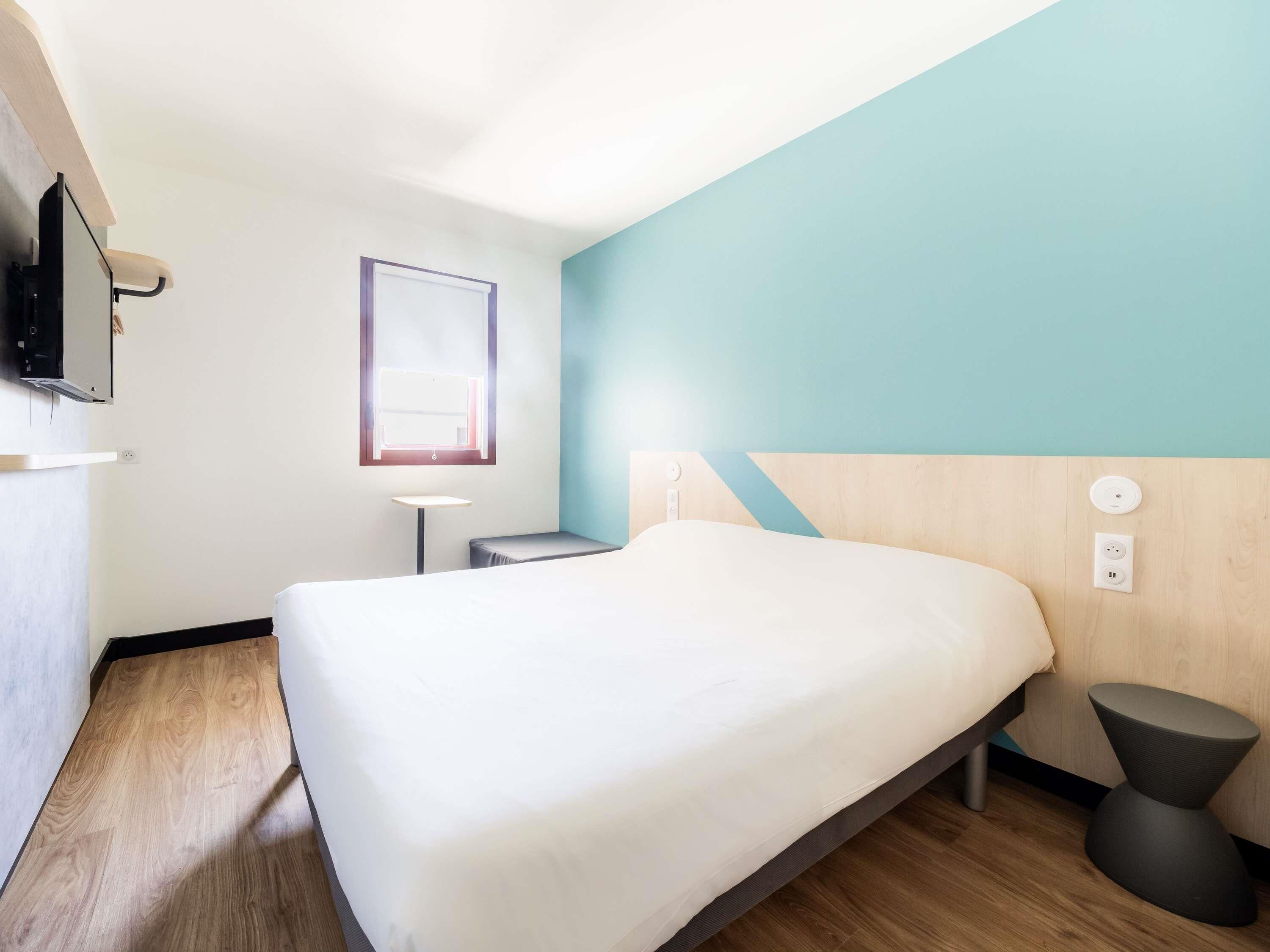 Une chambre d’hôtel équipée d’un lit, d’une table de chevet, d’une lampe et d’un téléviseur fixé au mur.