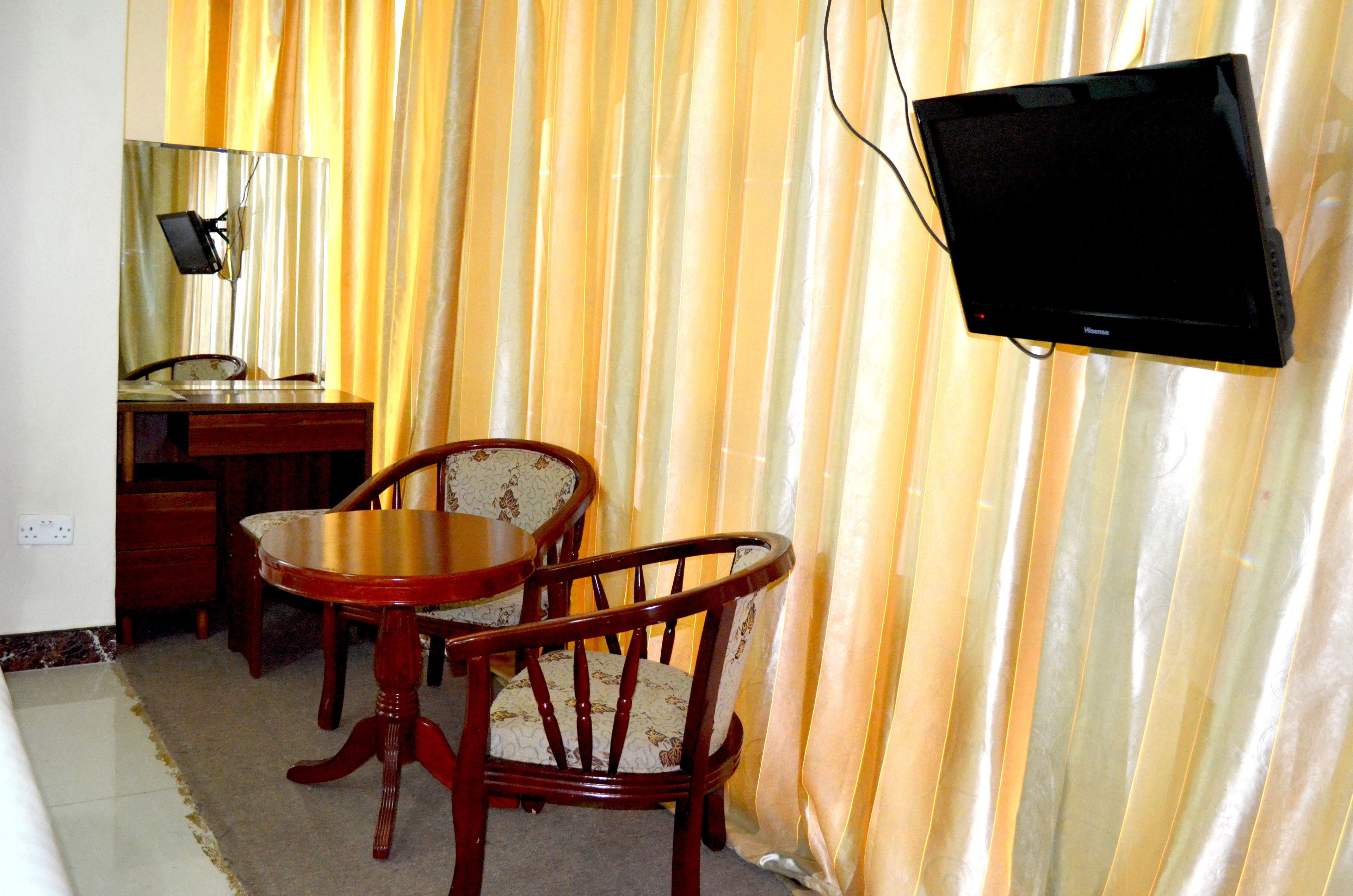 A room with a wooden desk, two chairs, a television mounted on the wall, and a curtain with a striped pattern.