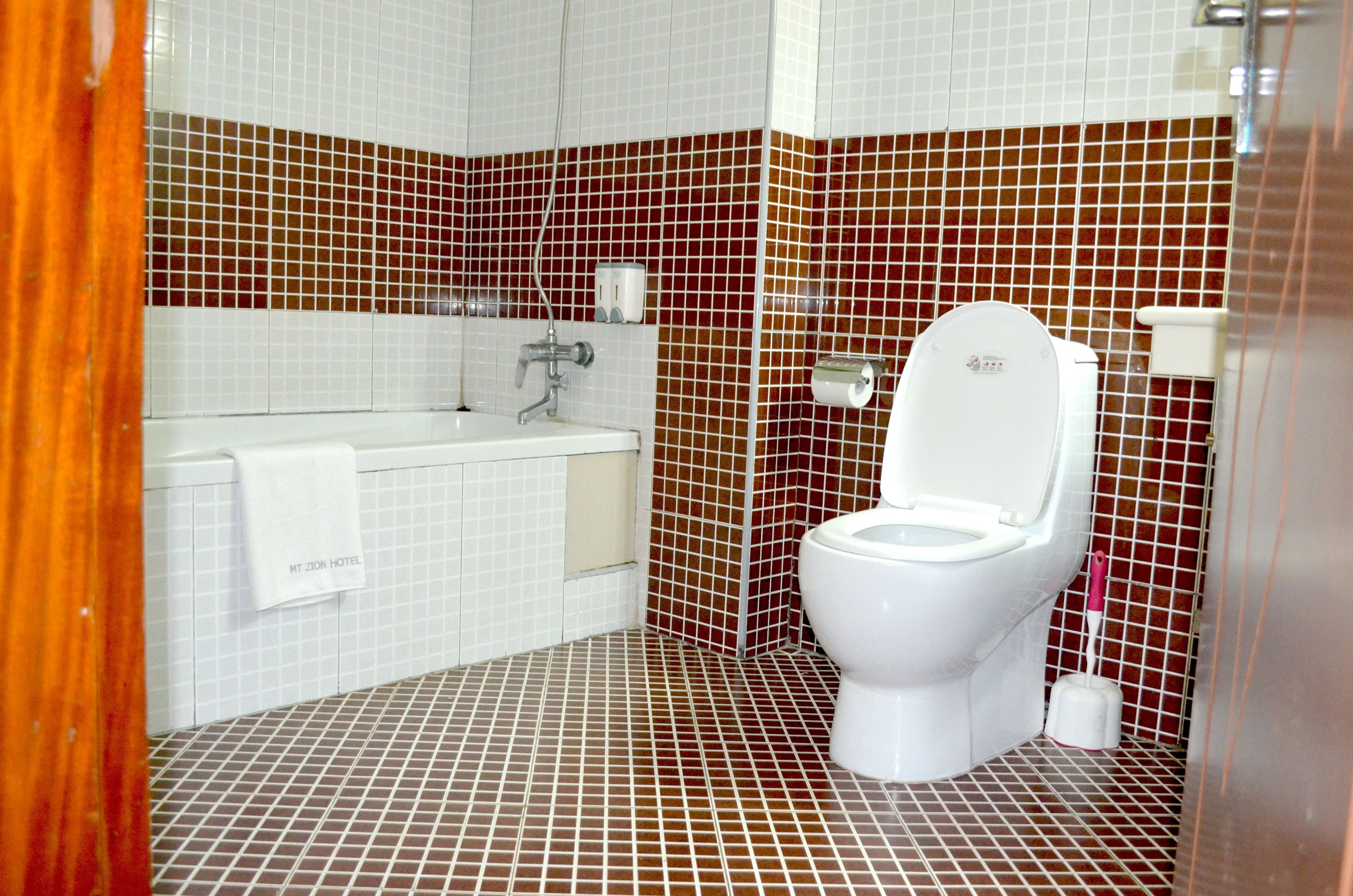 A bathroom with a white toilet, a sink, and a bathtub. The walls are tiled with a mix of white and brown tiles.