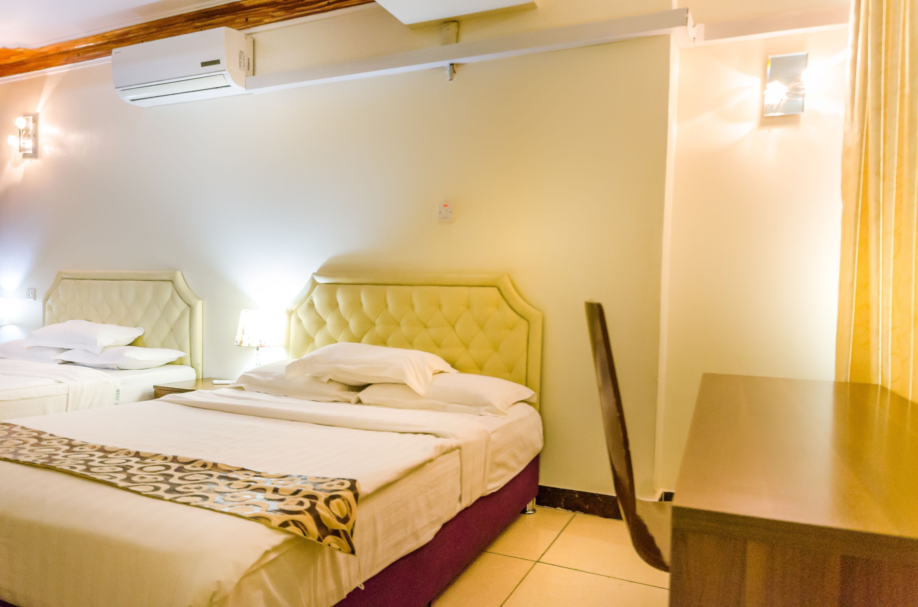 Habitación de hotel con dos camas, techo de madera, unidad de aire acondicionado y una mesita de noche.