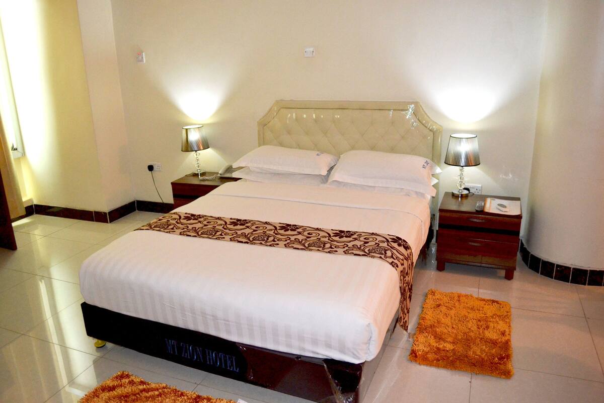 A hotel room with a large bed, two bedside tables, and two lamps.