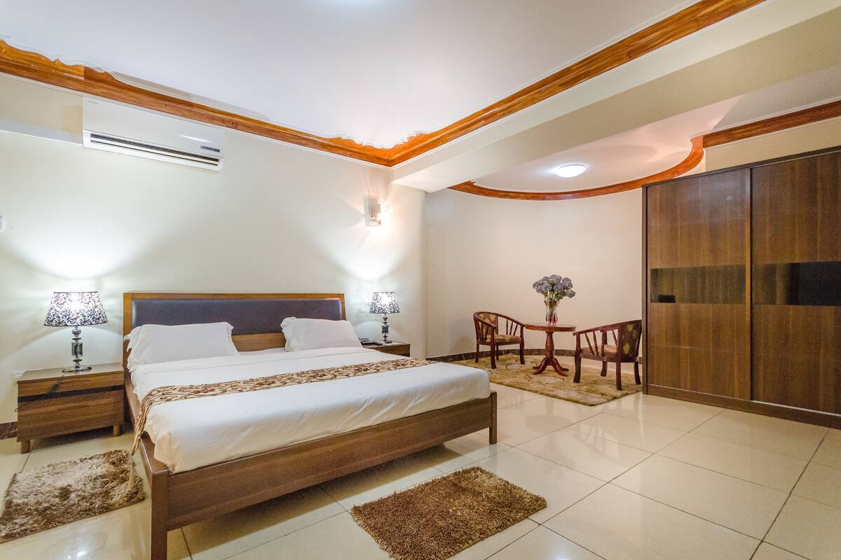 A bedroom with a wooden bed, bedside tables, a small table with chairs, and a wardrobe.
