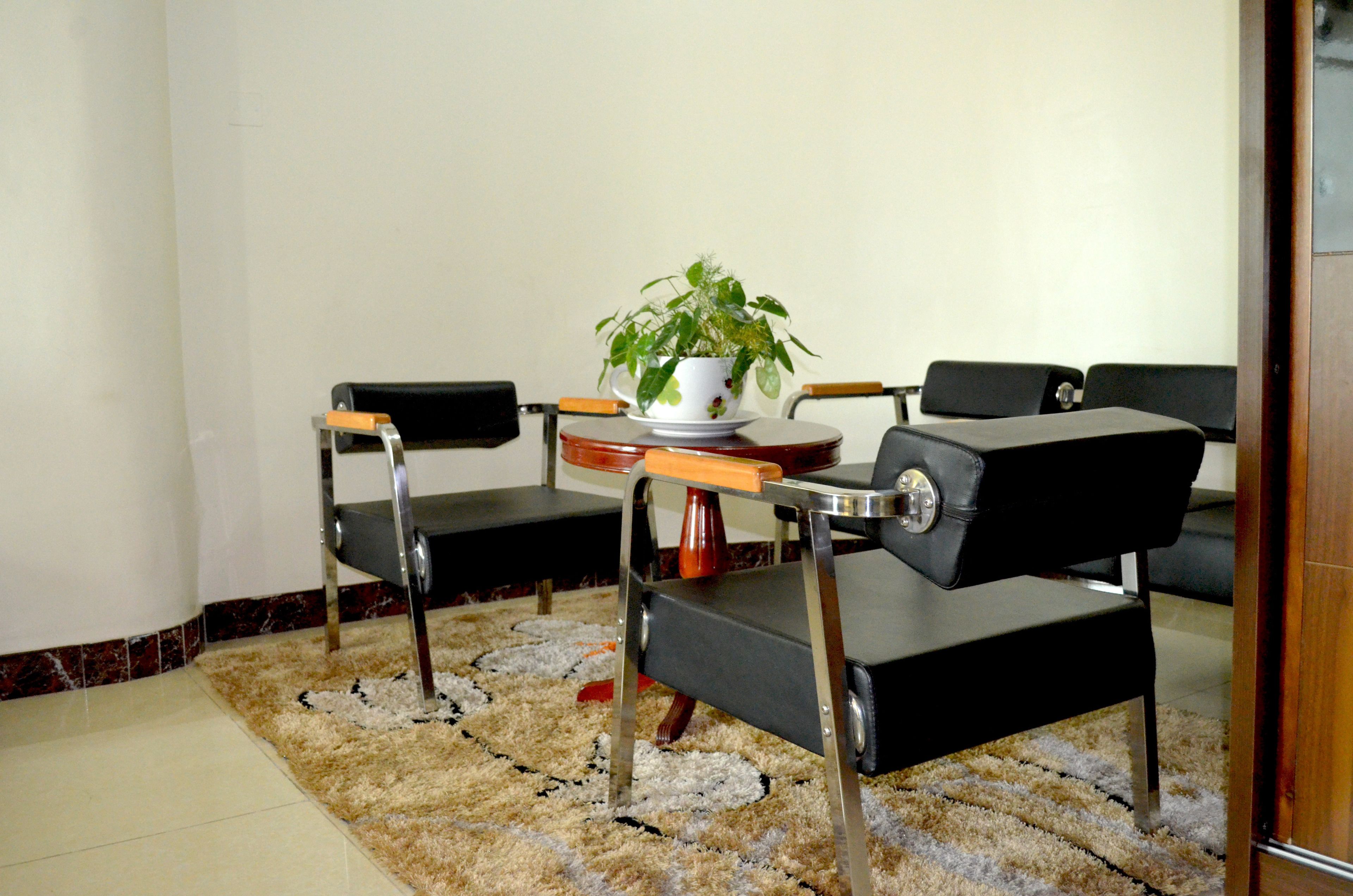 Una habitación con un sofá de cuero negro, una mesita redonda con una taza y platillo blancos, y una planta en maceta.