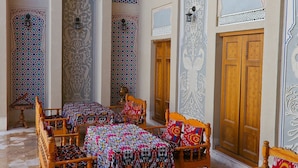 A traditional room with four wooden beds, each with colorful patterned bedspreads. The room features ornate wall decorations and wooden doors. - Hotel Fatima (Bukhara)