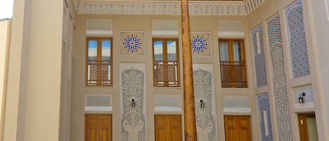 A courtyard with wooden benches, a central column, and intricately designed doors and windows.