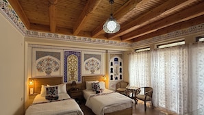 A room with two beds, a wooden ceiling, decorative wall panels, a small table, and a chair. - Hotel Fatima (Bukhara)