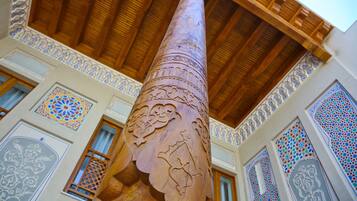 A tall, intricately carved wooden column in a building with detailed tile work and wooden beams on the ceiling.