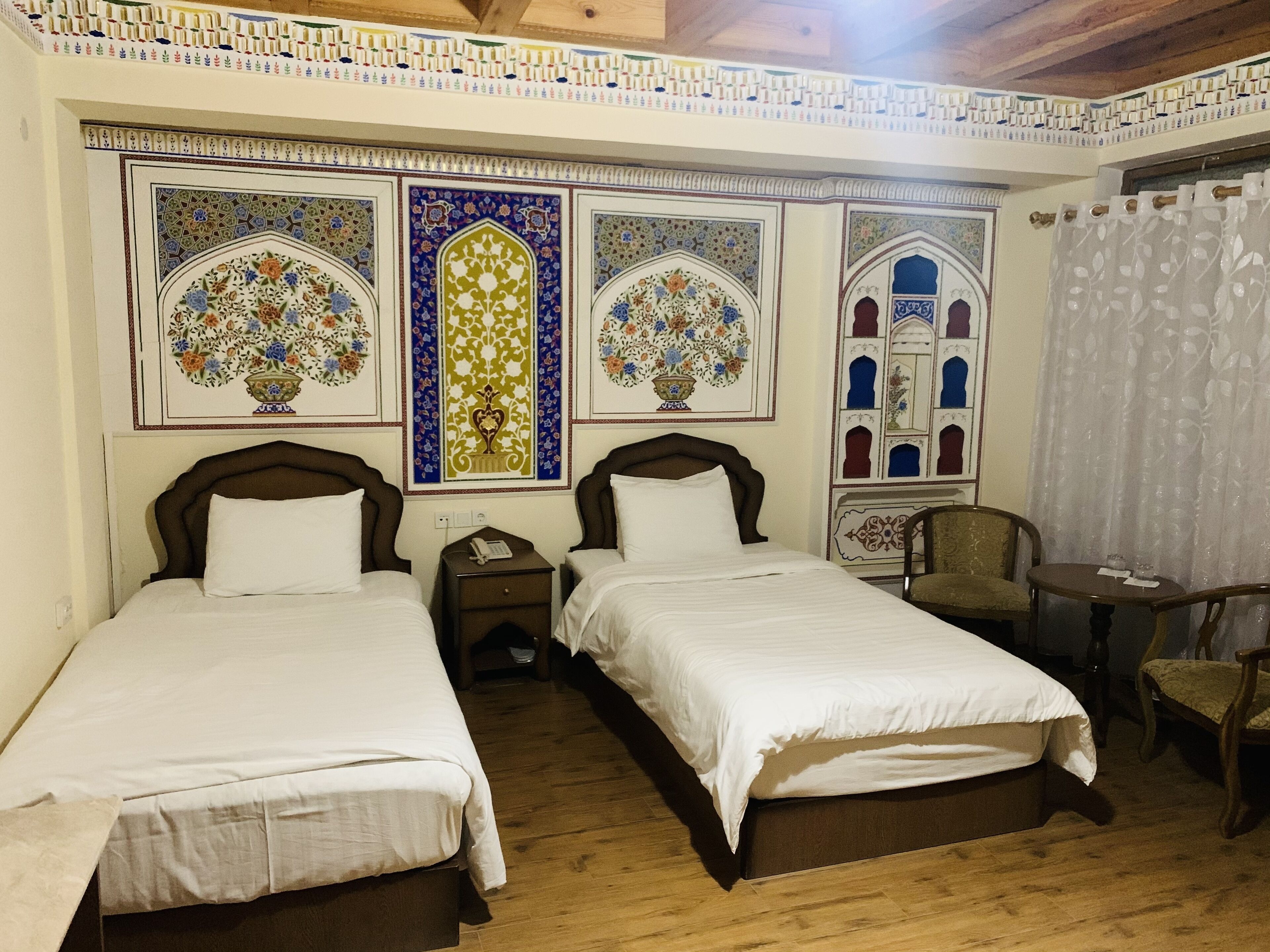 Una camera d'albergo con due letti, un tavolino, una sedia e pannelli decorativi alle pareti.