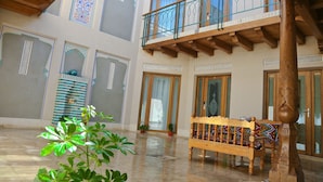 A spacious atrium with a wooden bench, potted plants, and a balcony with ornate railings. - Hotel Fatima (Bukhara)