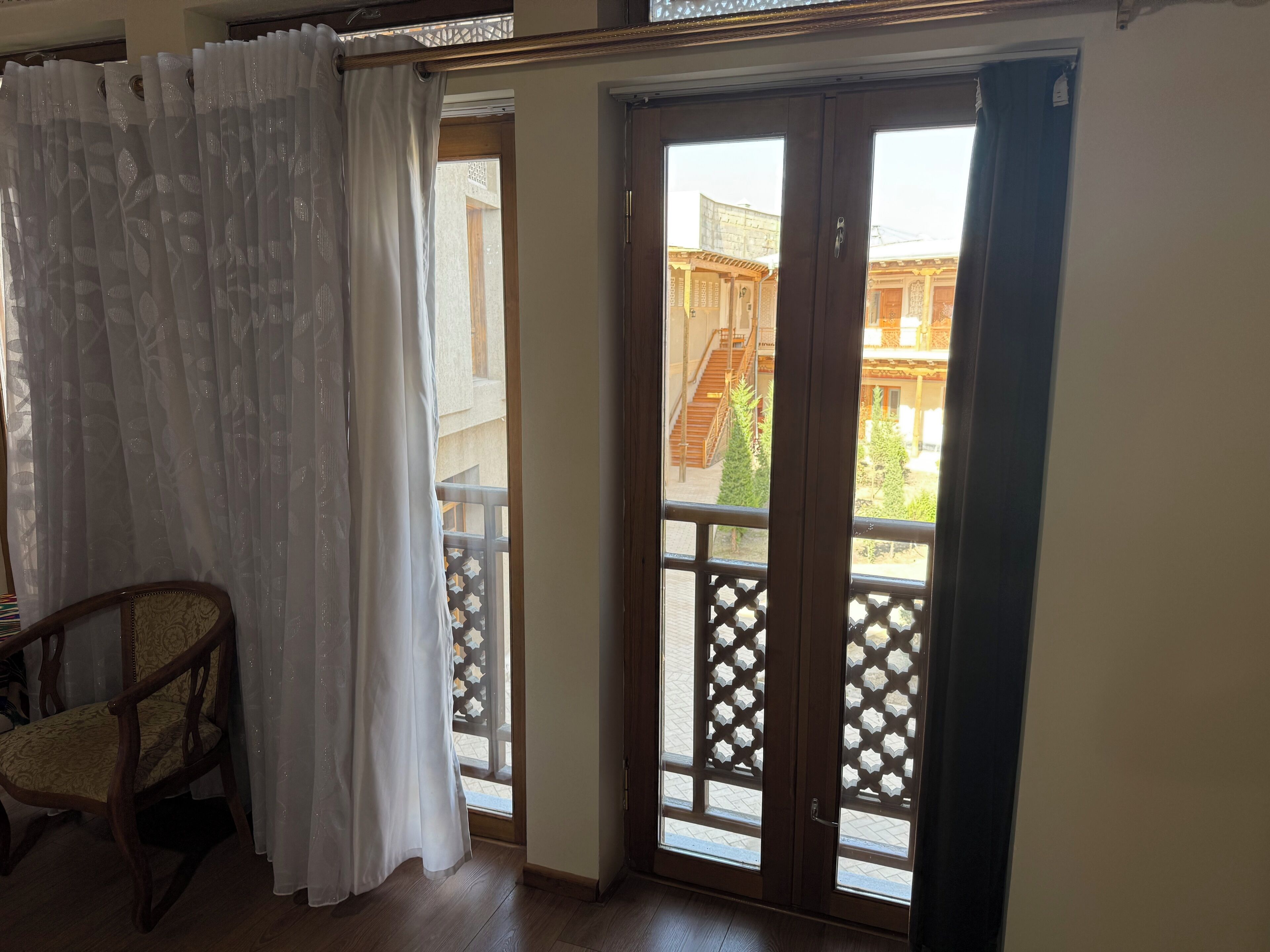 A room with a wooden chair, a sliding glass door leading to a balcony, and a view of traditional architecture outside.