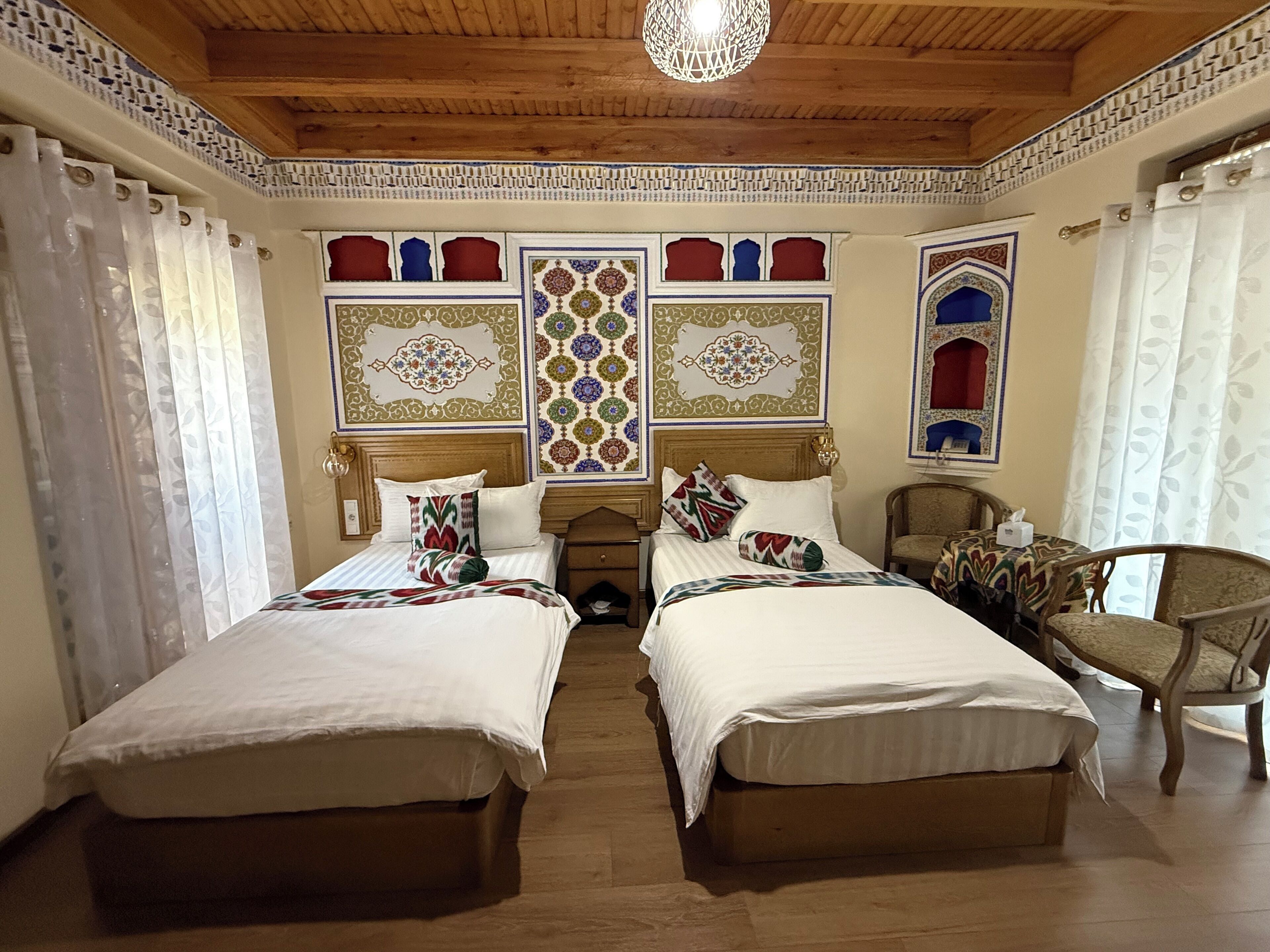 A hotel room with two beds, a wooden ceiling, decorative wall panels, and a chandelier.