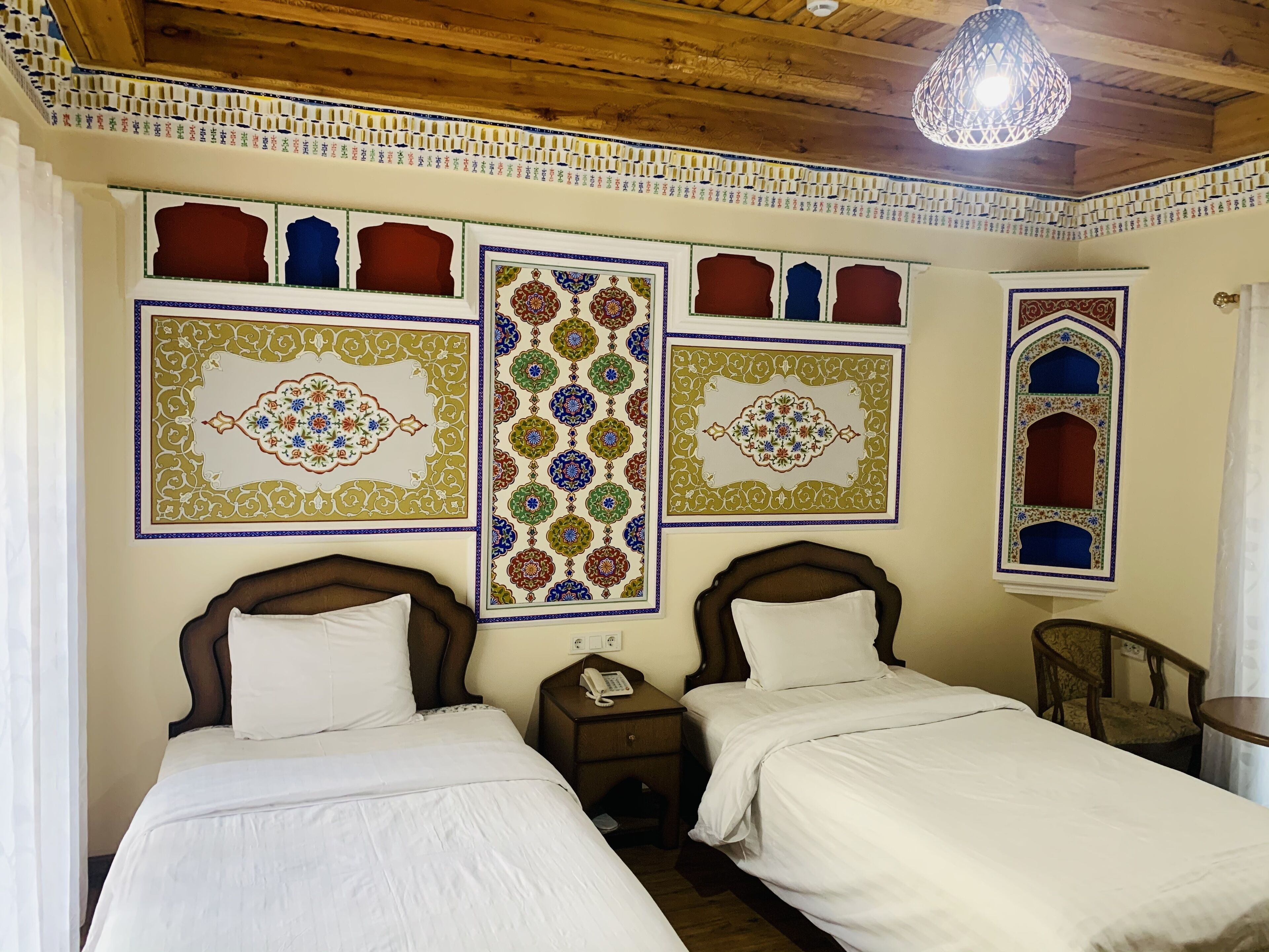 A room with two beds, a wooden ceiling, and decorative wall panels.