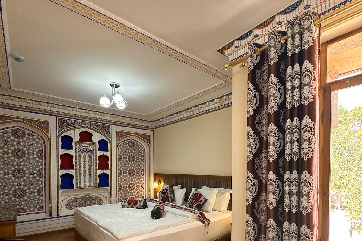 Ein Schlafzimmer mit Holzboden, einem Bett mit weißer Bettwäsche, gemusterten Vorhängen und dekorativen Wandverkleidungen.