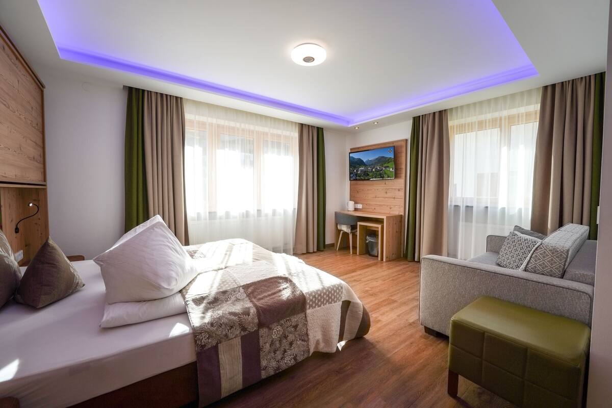A hotel room with a bed, a sofa, a desk, and a TV.