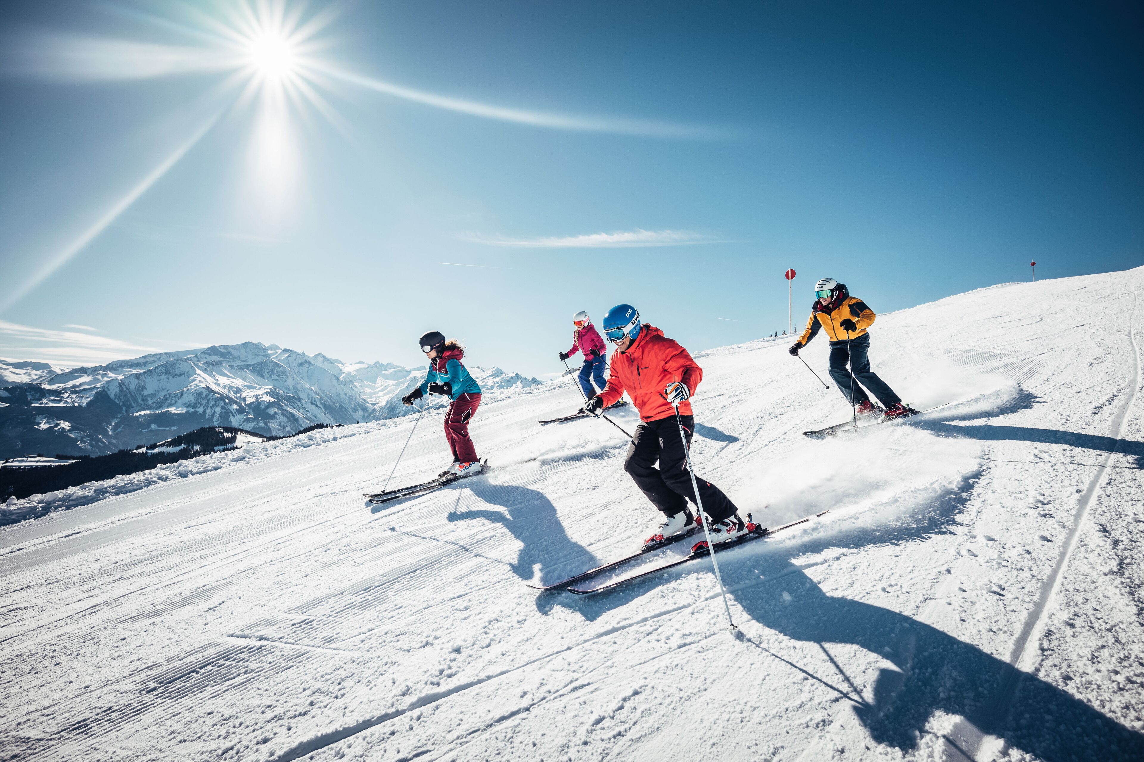 Een groep skiërs op een besneeuwde helling, met bergen op de achtergrond.