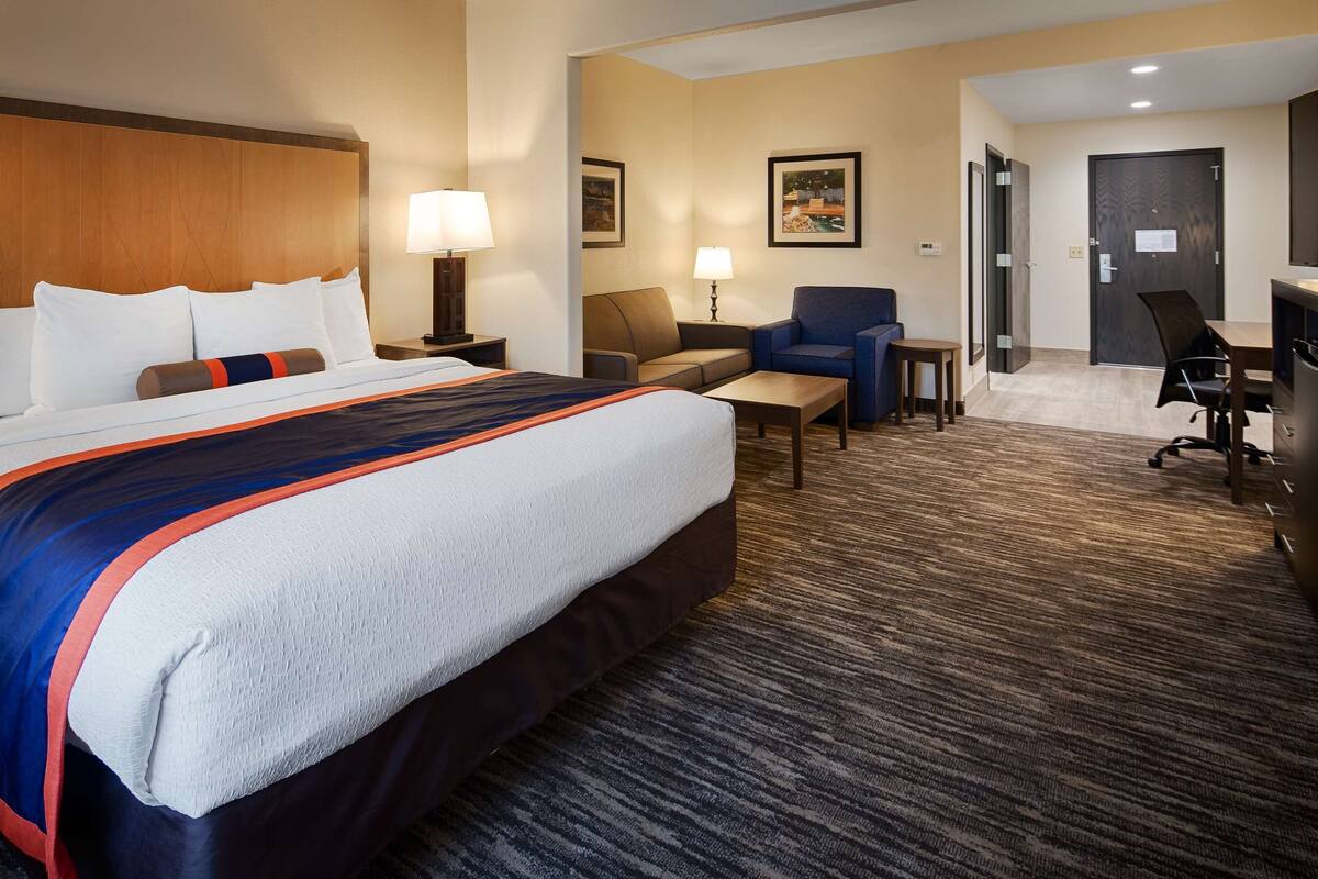 Ein Hotelzimmer mit einem großen Bett, einem Schreibtisch, einem Sessel, einer Couch und einer Schreibtischlampe.