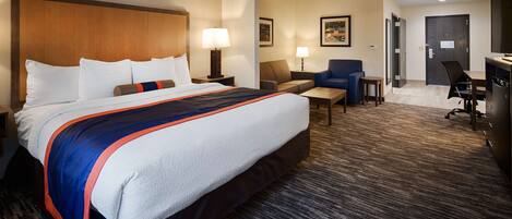 A hotel room with a large bed, a desk, a chair, a sofa, and a desk lamp.