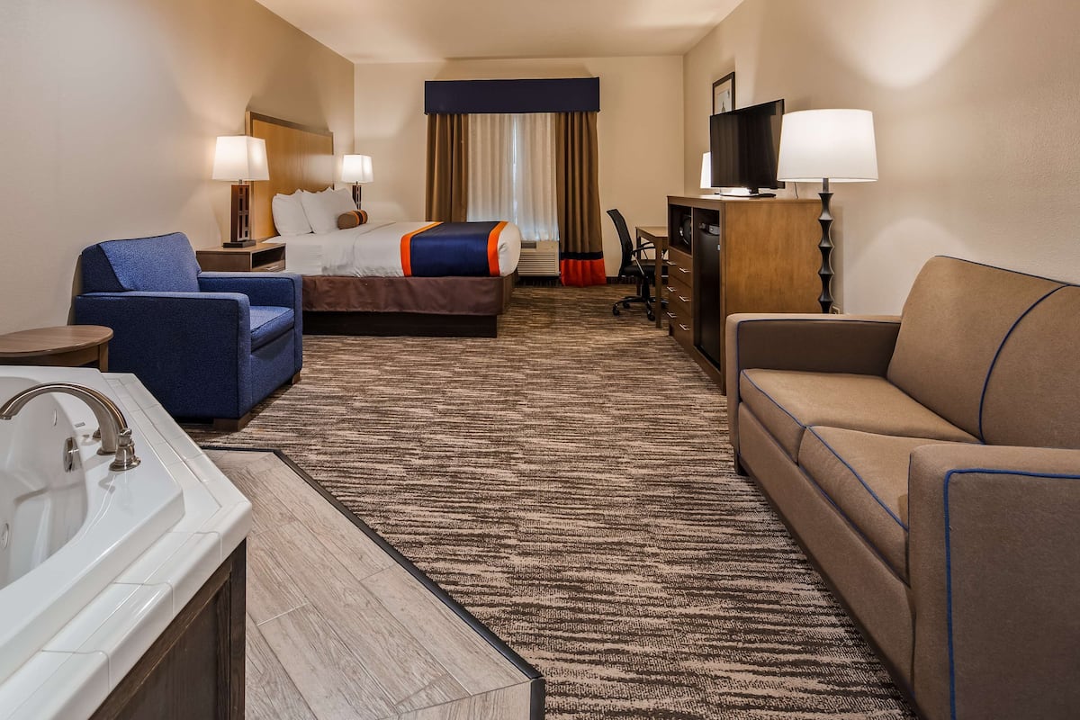 Ein Hotelzimmer mit einem großen Bett, einer Couch, einem Sessel, einem Schreibtisch, einem Fernseher, einer Lampe und einem Badezimmer mit Badewanne und Waschbecken.