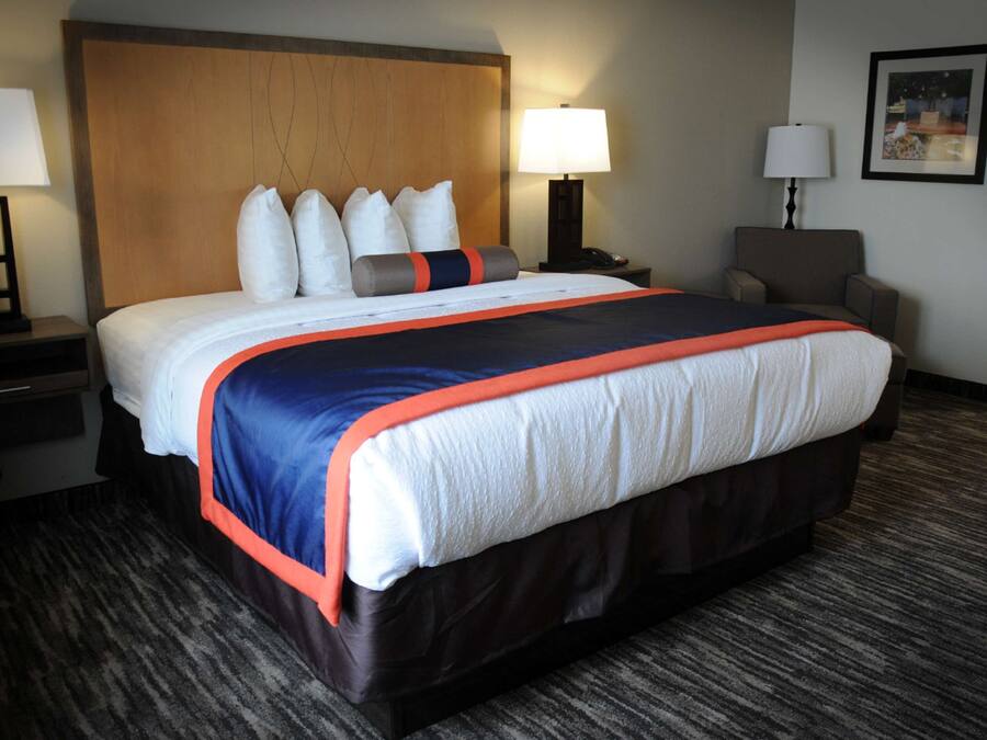 A hotel room with a large bed, two bedside tables with lamps, a chair, and a framed picture on the wall.