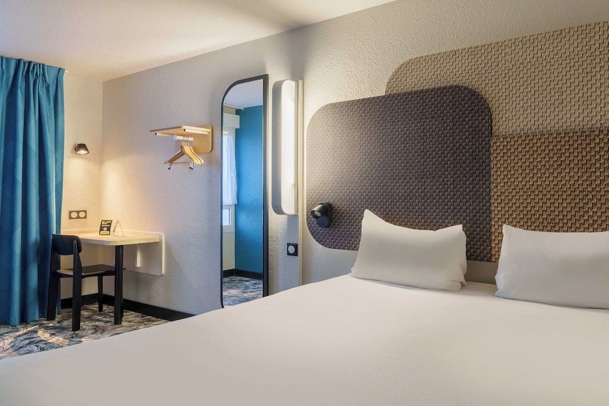 Ein Hotelzimmer mit einem großen Bett, einem Schreibtisch mit Stuhl, einem Spiegel und einer Wandleuchte.