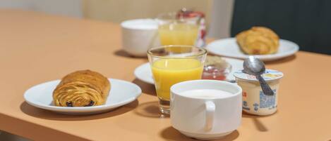 Desayuno con cruasanes, jugo de naranja, leche y yogur sobre una mesa.