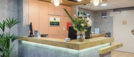 A reception desk with a wooden counter, a potted plant, and a wall-mounted sign.