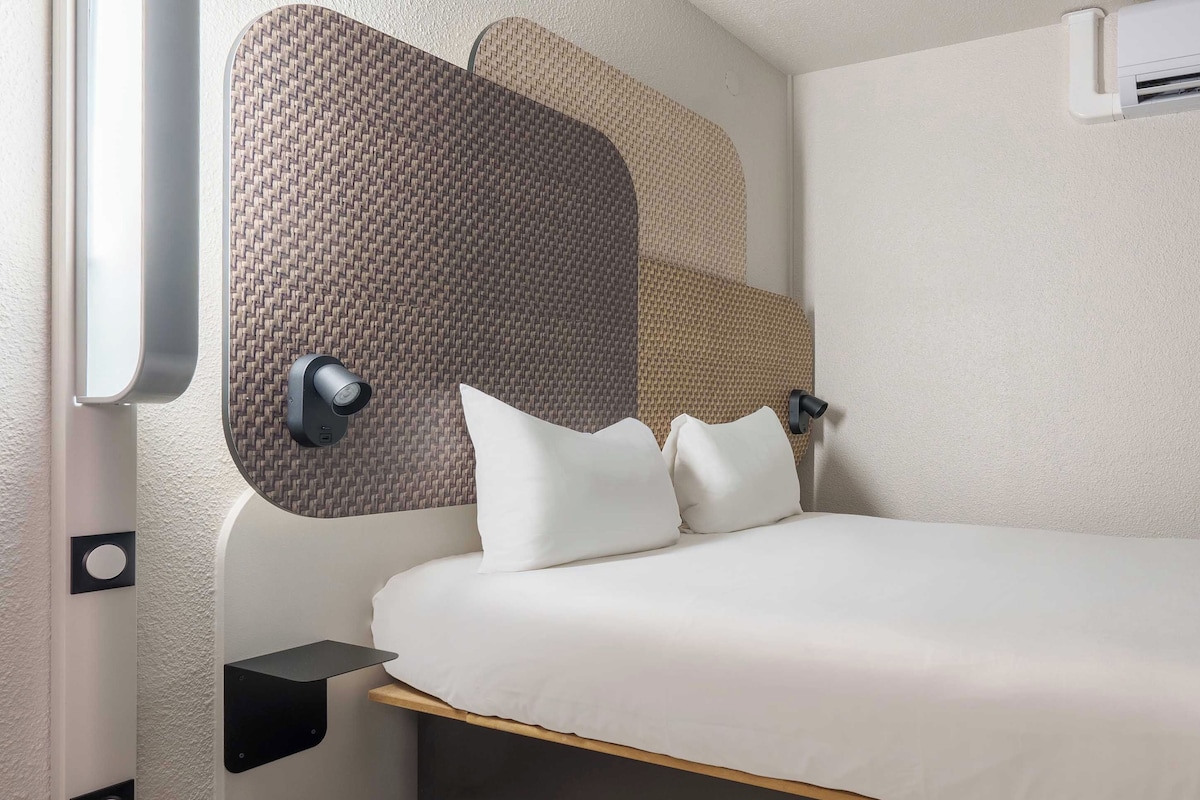 A compact room with a bed, a wall-mounted shelf, and a textured wall design.