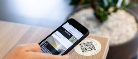 A smartphone displaying a hotel booking app with a QR code on a wooden surface.