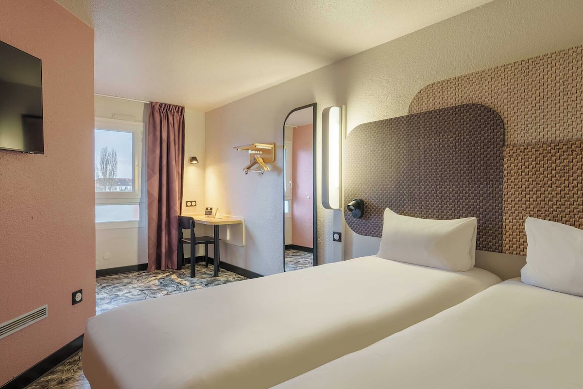 Ein Hotelzimmer mit einem großen Bett, einem Schreibtisch mit Stuhl, einem Fernseher und einem Fenster mit Vorhängen.